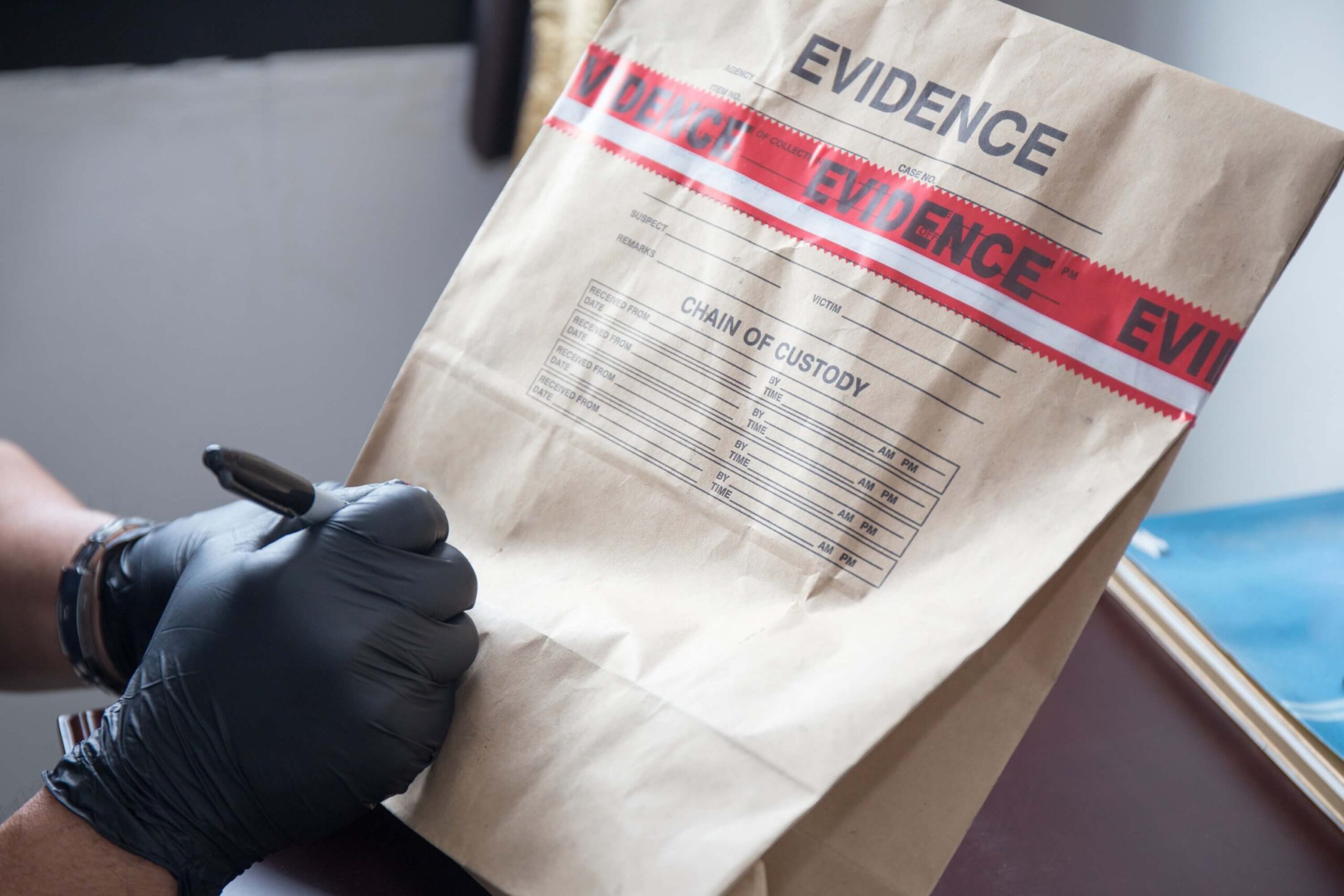 Forensic hand with black gloves writing on a sealed evidence bag